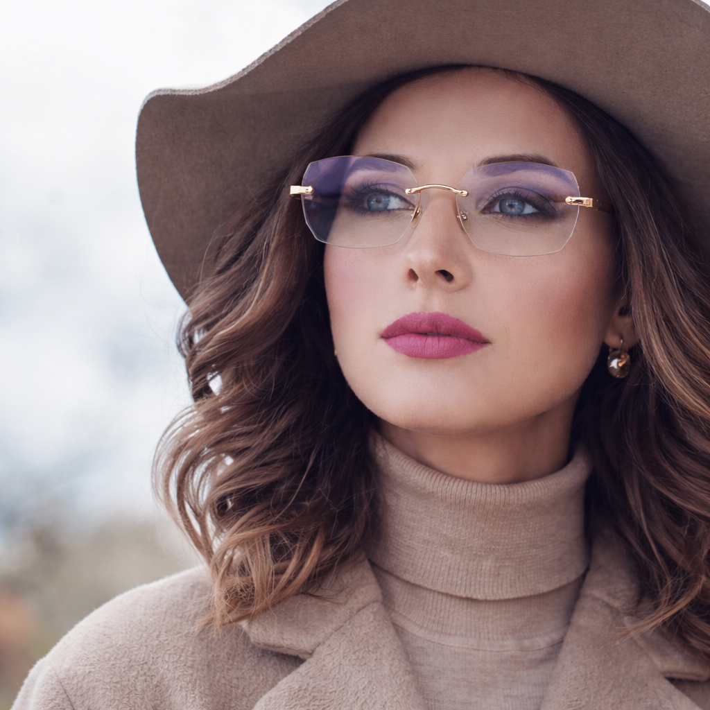 Elegant woman wearing a wide-brimmed hat and trendy glasses, posing outdoors with a confident expression.
