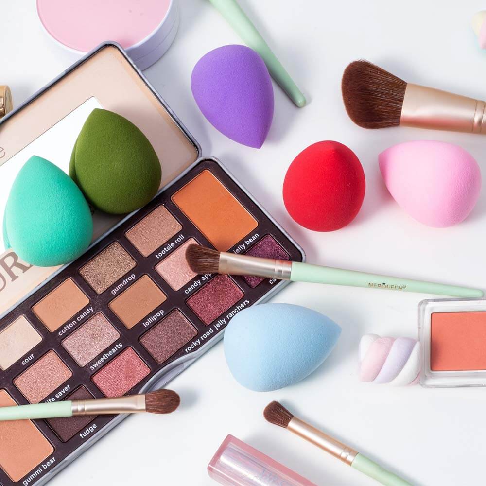 Axiva Perfect Blender – Flawless Makeup Sponge surrounded by beauty products and makeup brushes on a flat surface.